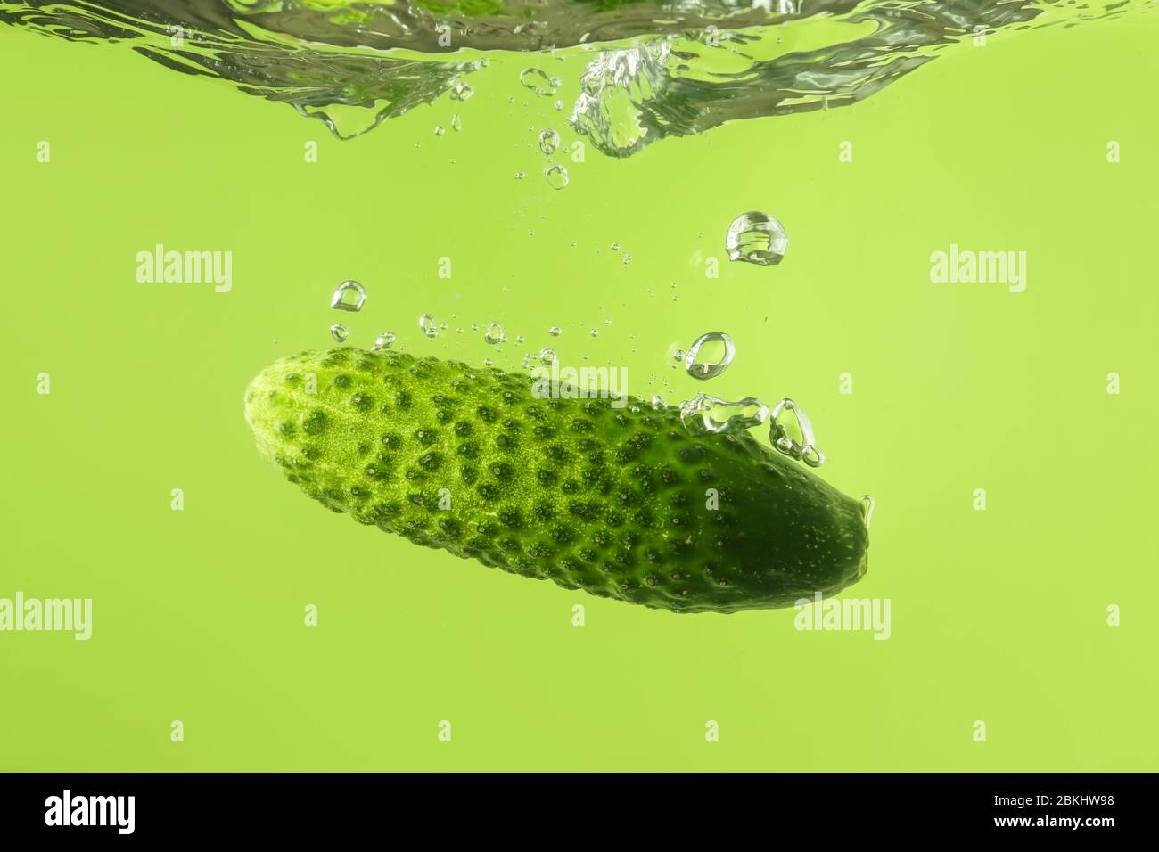 Falling of fresh cucumber into water against color background Stock