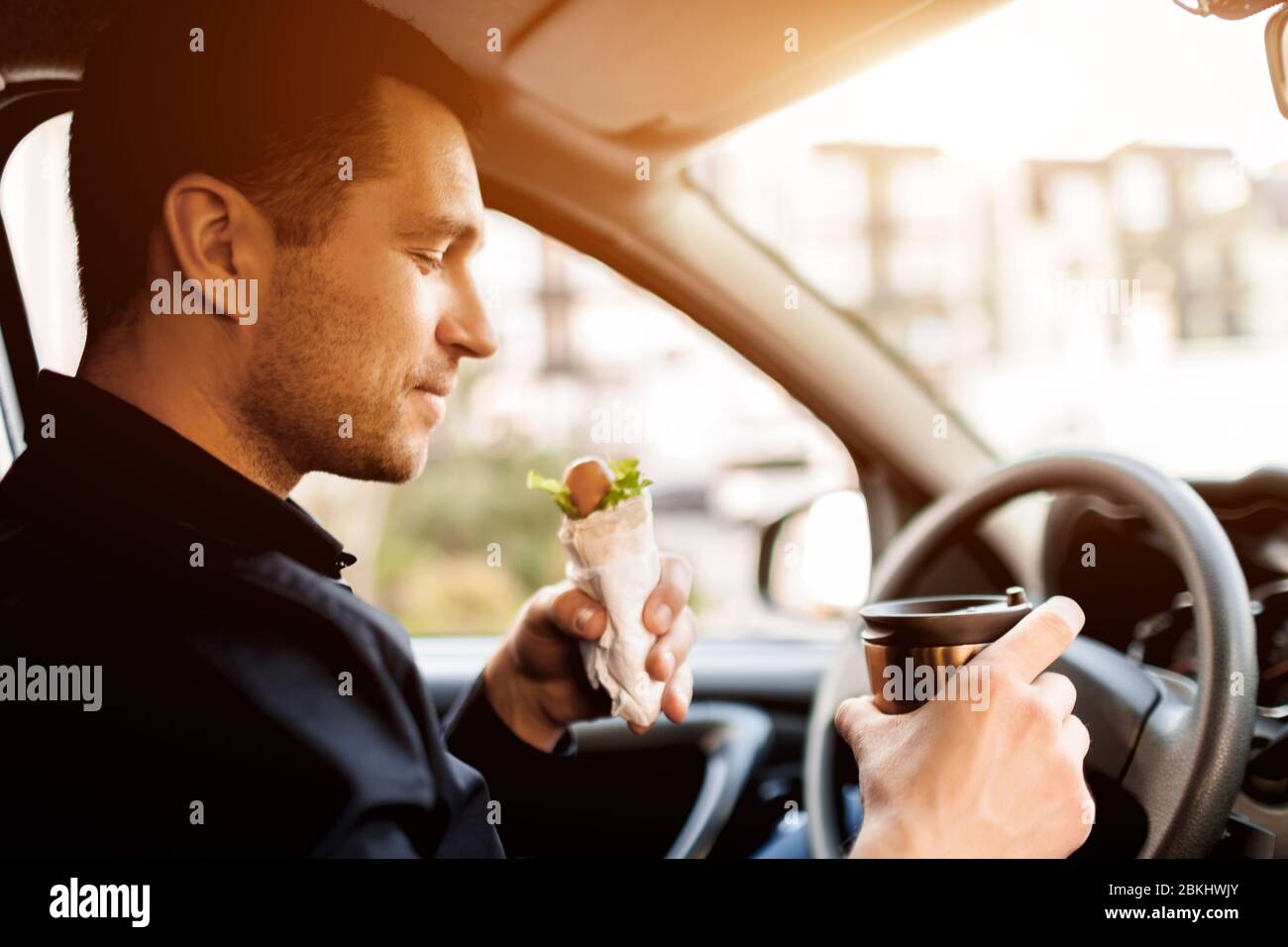 Stopping for a bite to eat . Man eat snack in the car and drinks coffee