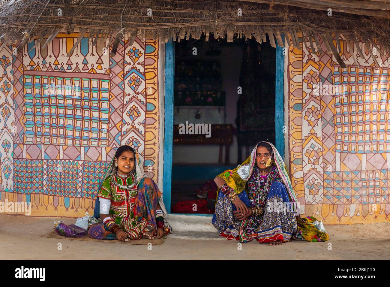 India, Gujarat State, Kutch region, Ludiya village, near Bhuj, Meghwal tribe women wearing traditional embroidered clothes in front of a decorated hut Stock Photo