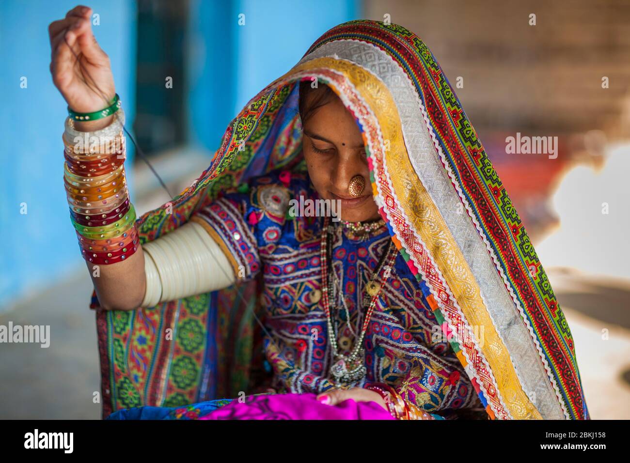 India, Gujarat State, Kutch region, Ludiya village, near Bhuj, woman of the Meghwal tribe in traditional clothes embroidering in front of the blue wall of a hut Stock Photo