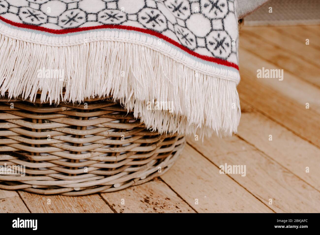 Cream luxury fringed blanket draped over wicker basket, hygge concept, warmth home concept homely, nice things, homeware, wooden floor, living concept Stock Photo