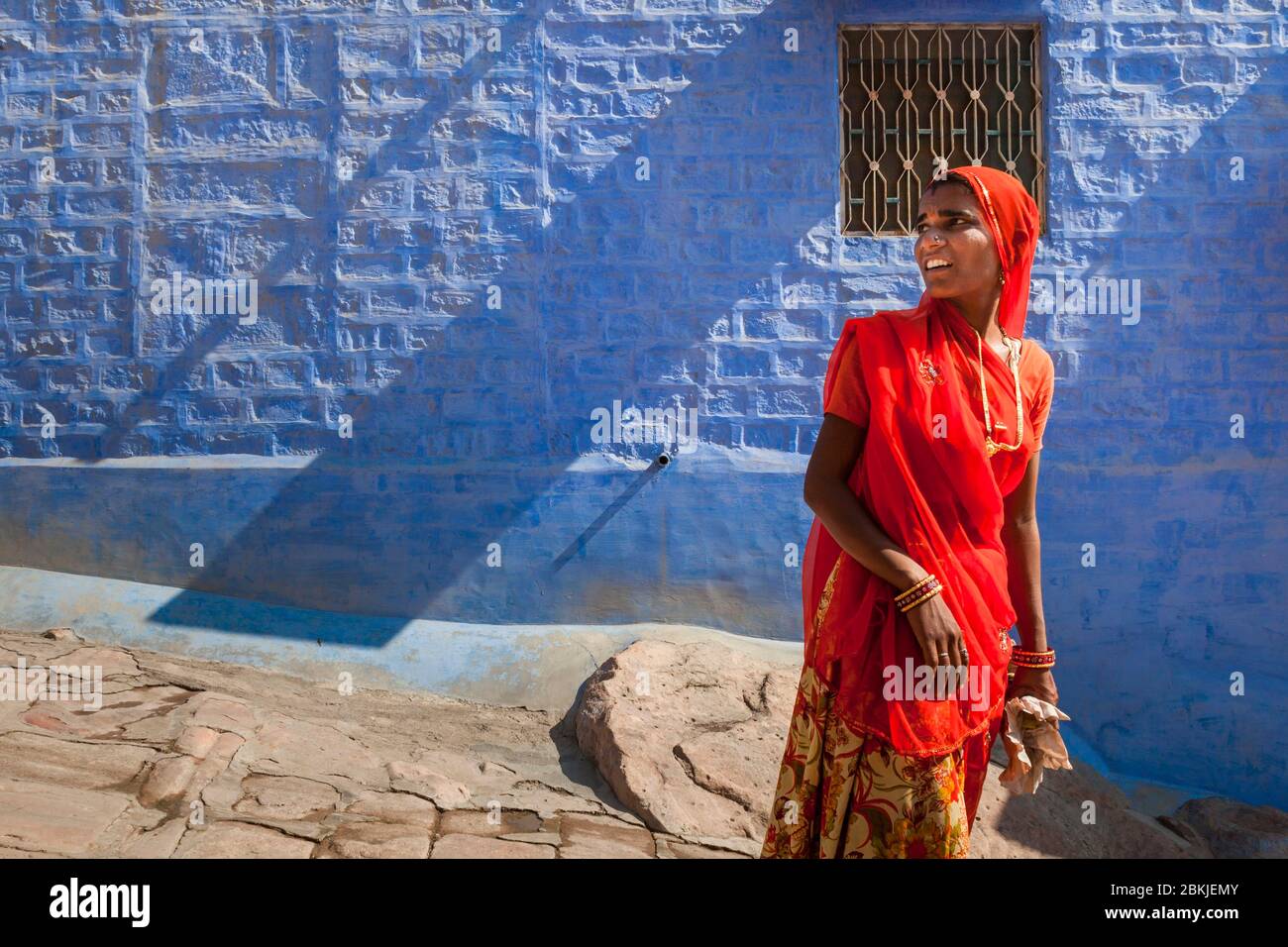 India, Rajasthan, Jodhpur, young woman in red sari walking by a blue house Stock Photo
