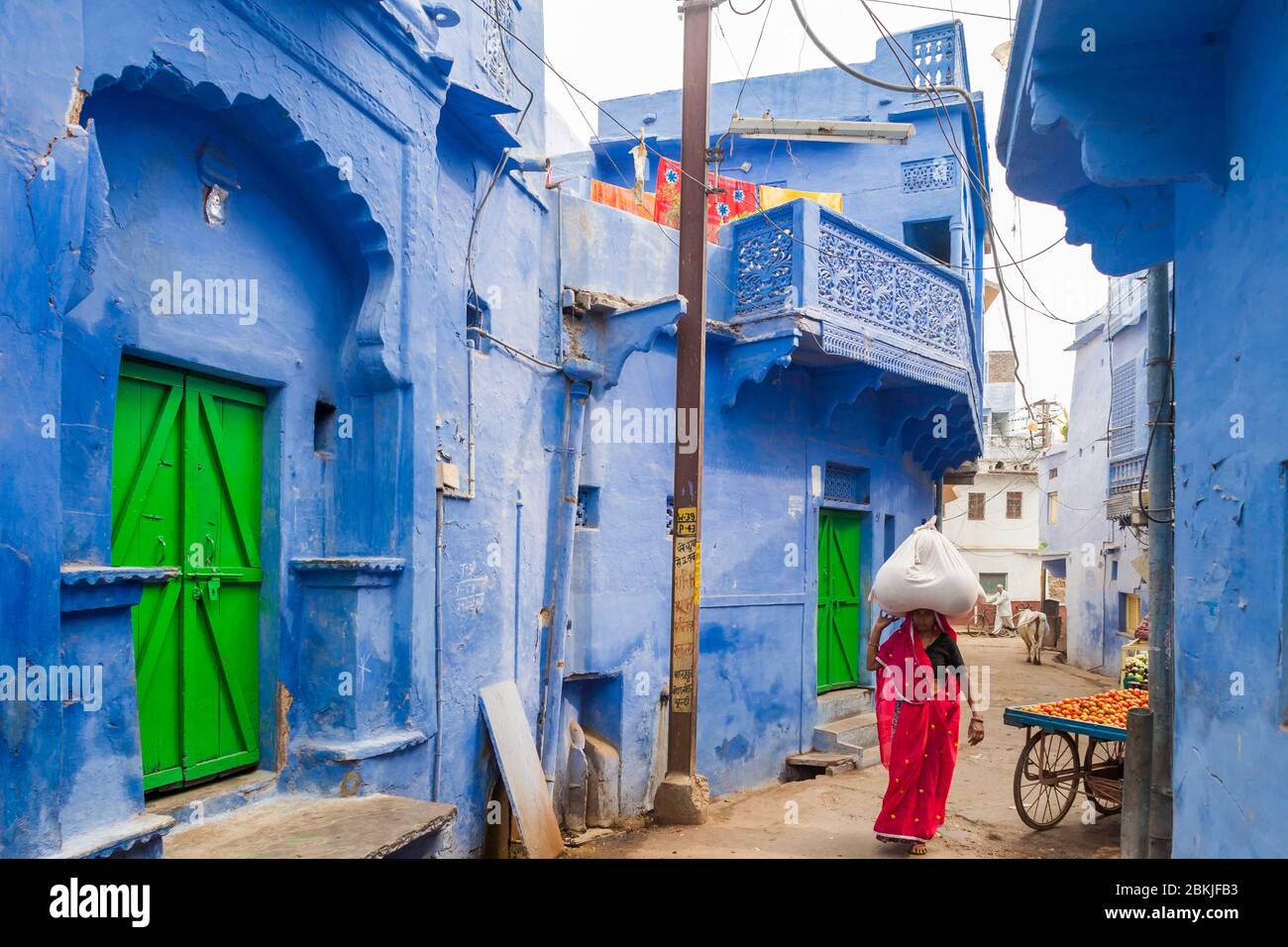 India, Rajasthan, Bundi, woman carrying a bag on her head and dressed with a red sari walking in a blue painted street Stock Photo