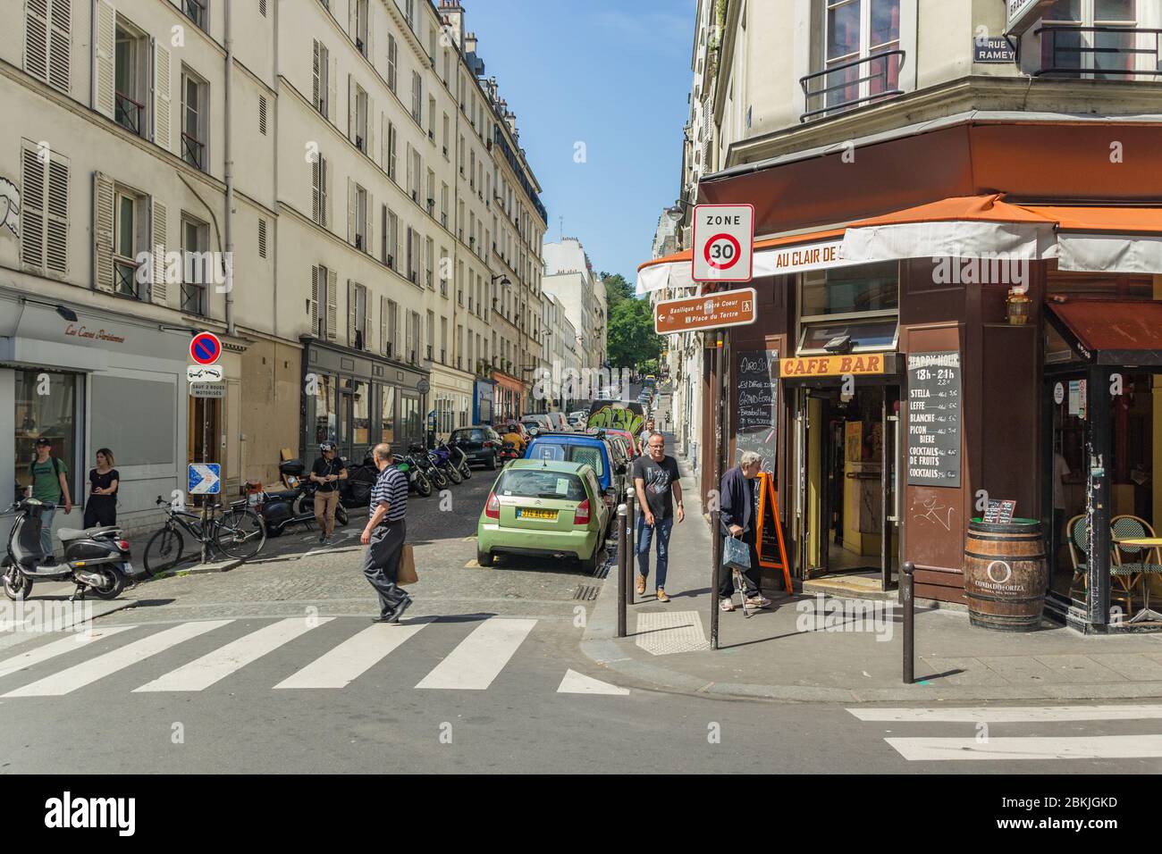 Paris, France - June 23, 2016: Quiet and cozy street of Paris near Montmartre. Nearly parked cars and motorbikes along narrow paving stones and locals Stock Photo