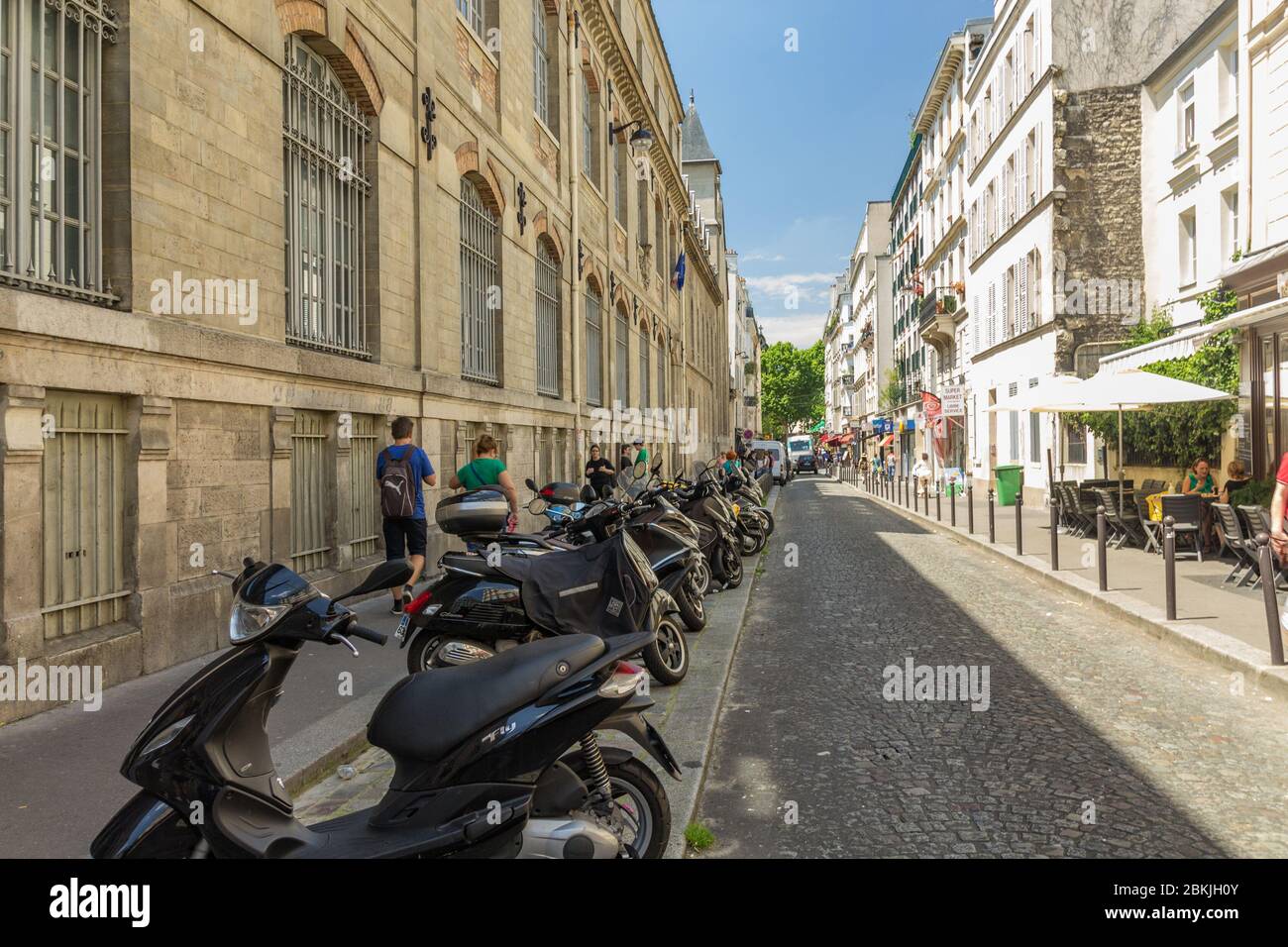 Paris, France - June 23, 2016: Quiet and cozy street of Paris near Montmartre. Nearly parked cars and motorbikes along narrow paving stones and locals Stock Photo