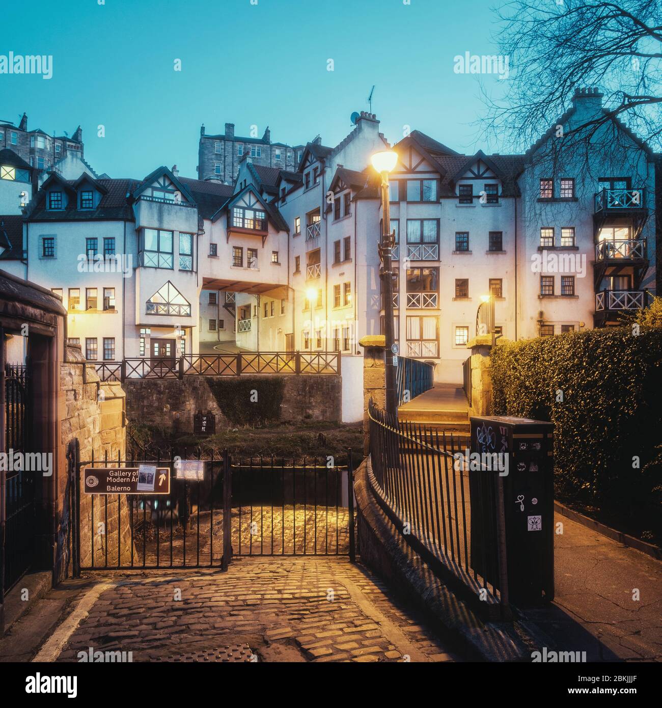 View on old houses and a street lit by yellow light from street lamps in  Dean village and the bridge cross Leith river. In the evening, blue hour.  New Town part of
