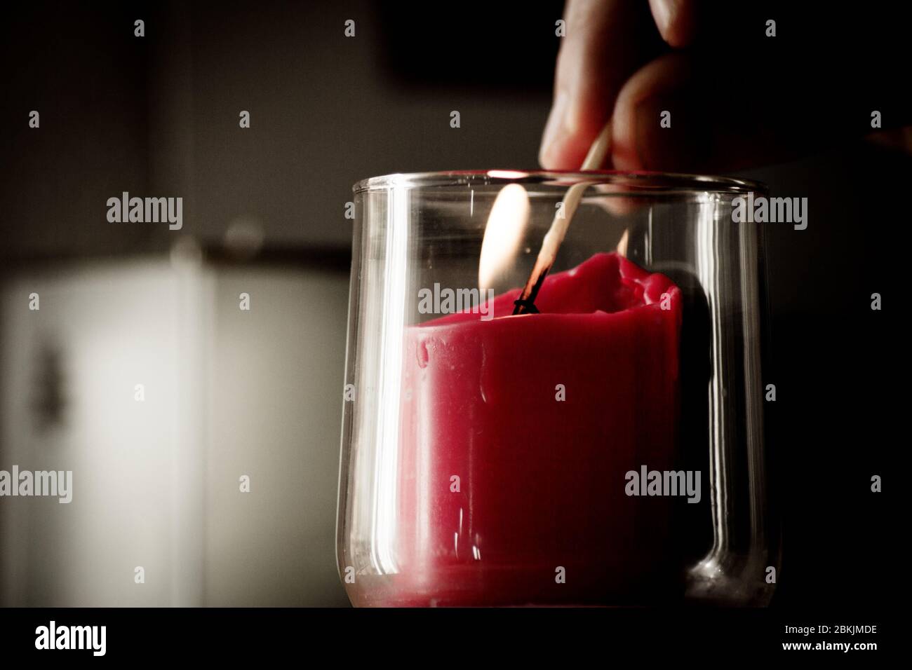 Fingers of man lighting a red candle inside a transparent glass vase