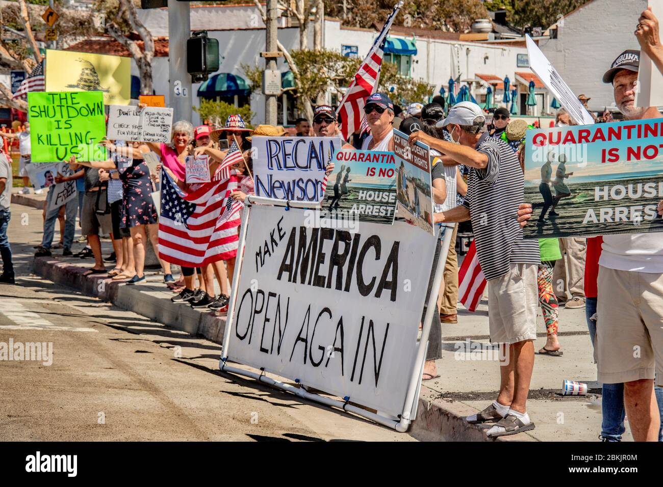 Affecting a patriotic pose, multiracial protesters opposing California Governor Gavin Newsom's statewide lockdown order to combat the coronavirus/COVID-19 pandemic gather on Pacific Coast Highway in Laguna Beach, CA. Stock Photo