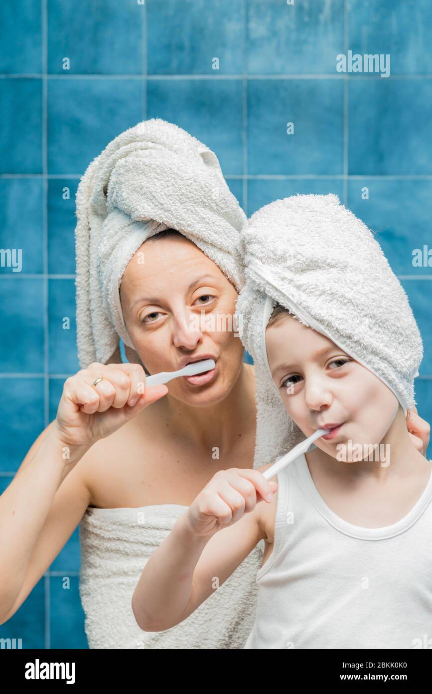 A woman and a boy with towels on their heads brushing their teeth Stock