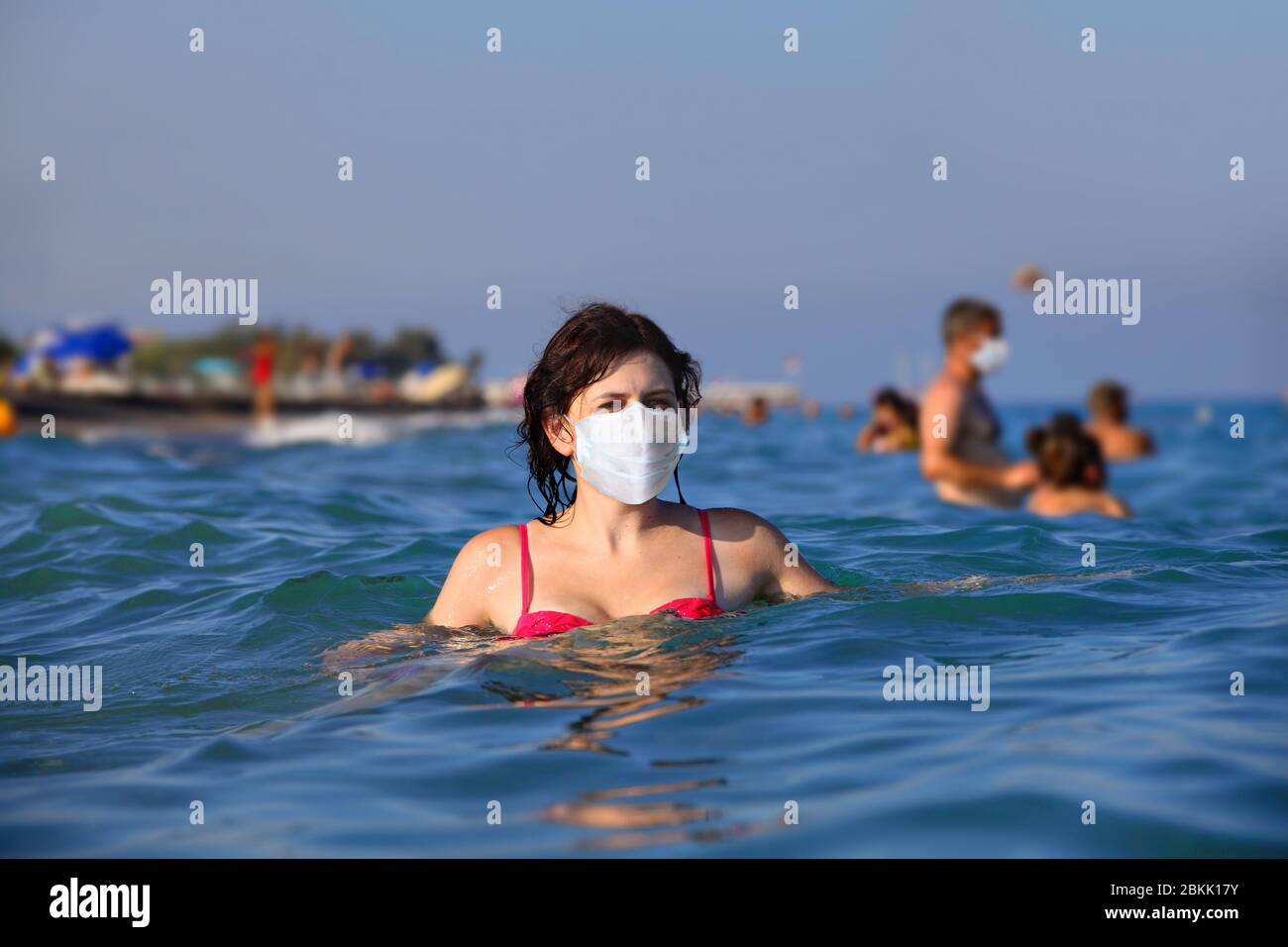 Young caucasian woman basking in the sea in a protective face mask. A beautiful female uses personal protective equipment during the Covid-19 pandemic Stock Photo
