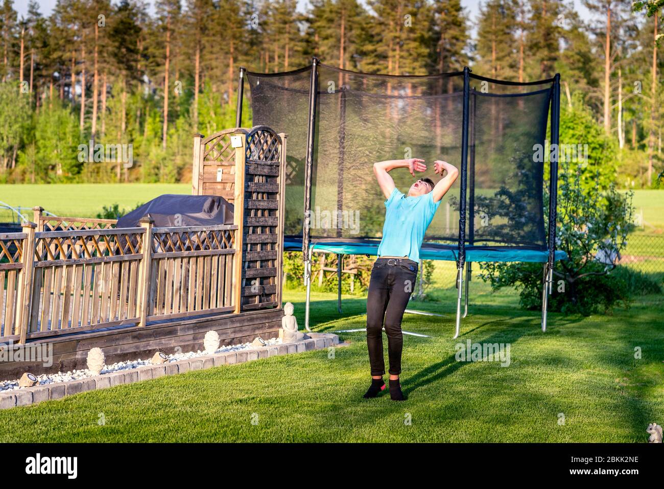 Young well trained sporty teenager starting acrobatic exercise salto - starting flip backwards. Exercise on green grass near wooden terrace fence and Stock Photo
