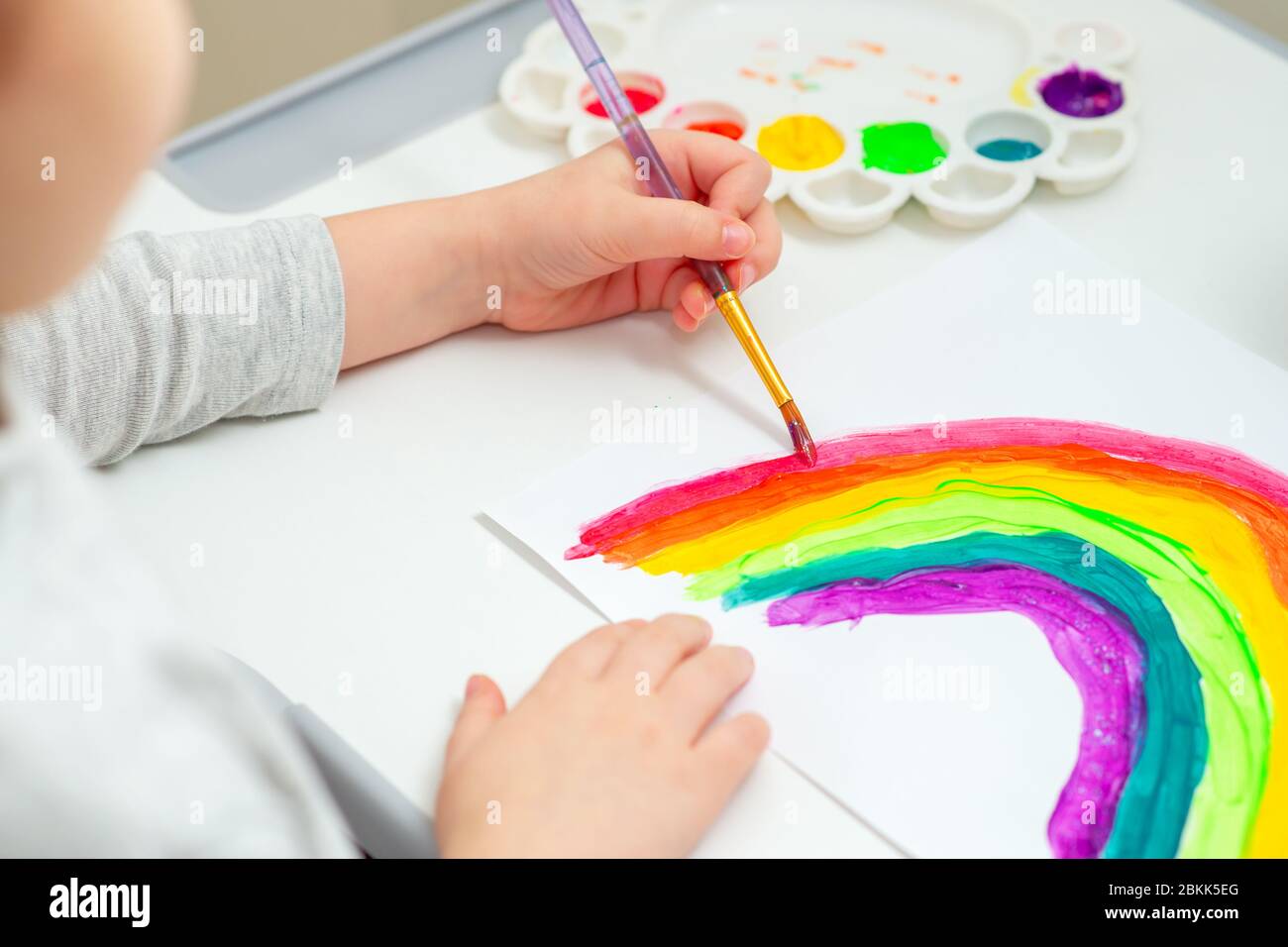 Child is drawing rainbow with watercolors on the sheet of paper. Children creativity. Stock Photo