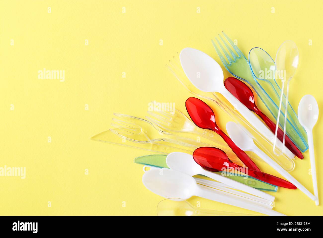 Plastic cutlery, forks, spoons and knives on yellow background. Pollution of the environment with plastic and microplastics. Copy space Stock Photo