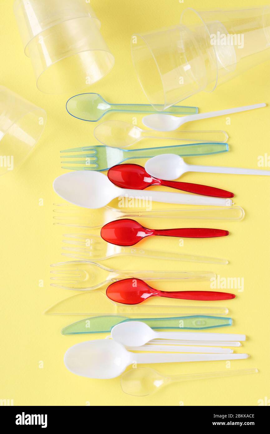 Set of color plastic cutlery and clear cups on yellow background. Pollution of the environment with plastic and microplastic. Vertical format Stock Photo