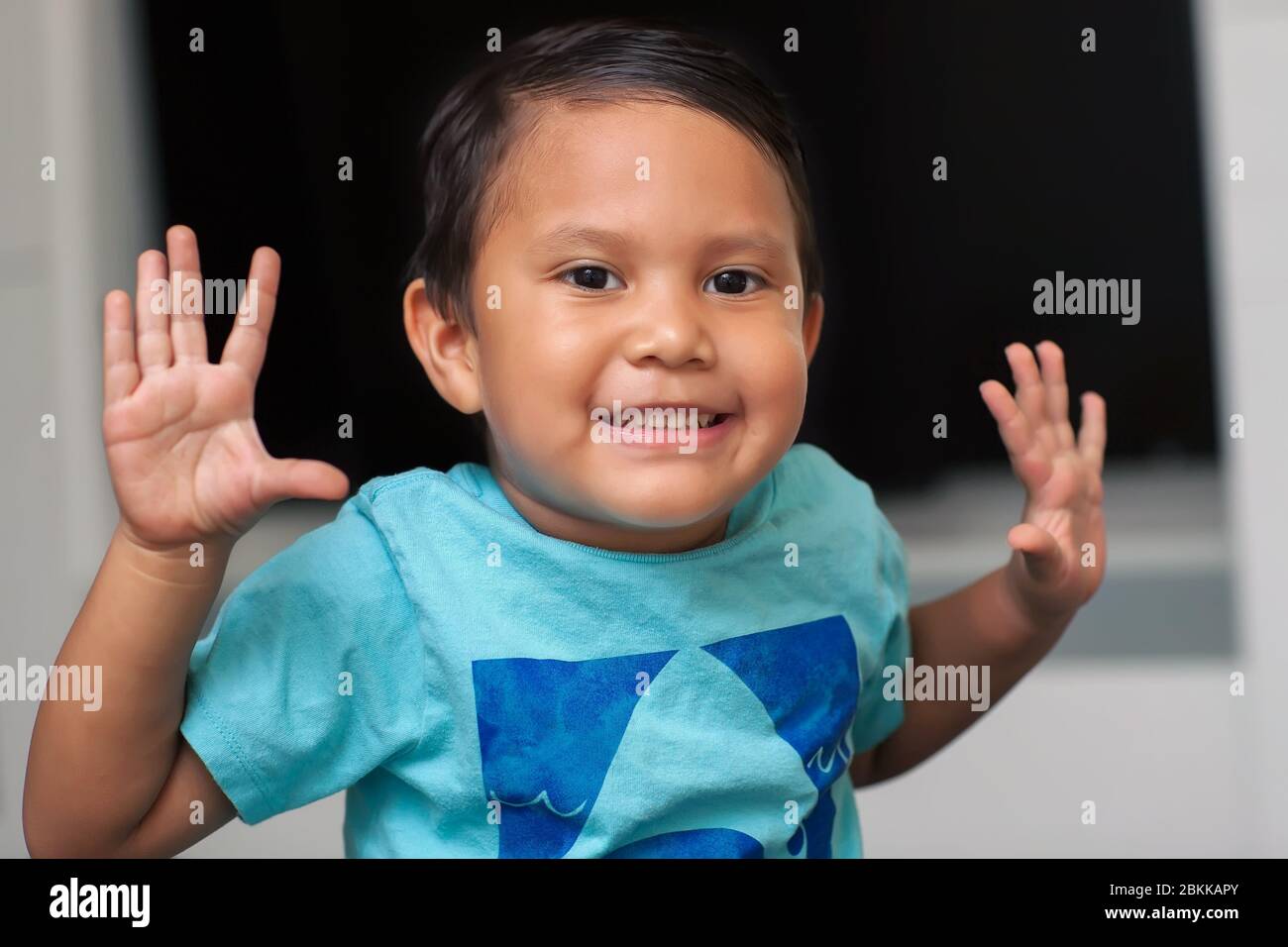 Young boy who is using his hands and fingers while learning to count, age of a  preschooler and raising both hands up while smiling. Stock Photo