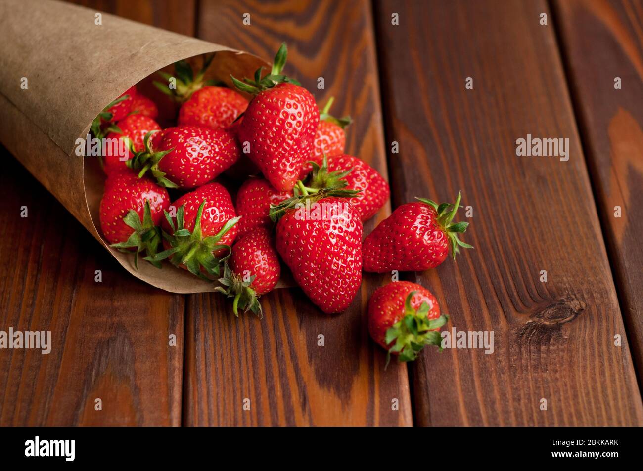Ripe strawberries in craft paper on a wooden background. Healthy fresh food. Top view Stock Photo
