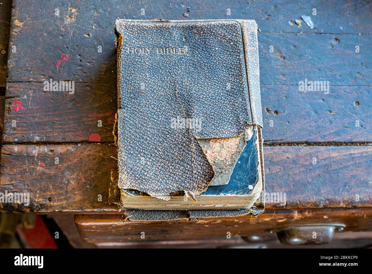 An old, tattered Holy Bible sitting on a wooden bench in an old workshop Stock Photo