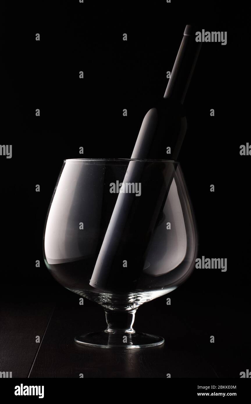 Black glass wine bottle in the huge wine glass isolated on the black background Stock Photo