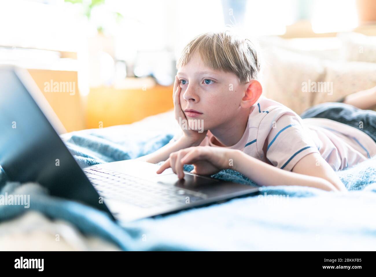 Tween working on laptop looking bored at home on sunny day Stock Photo
