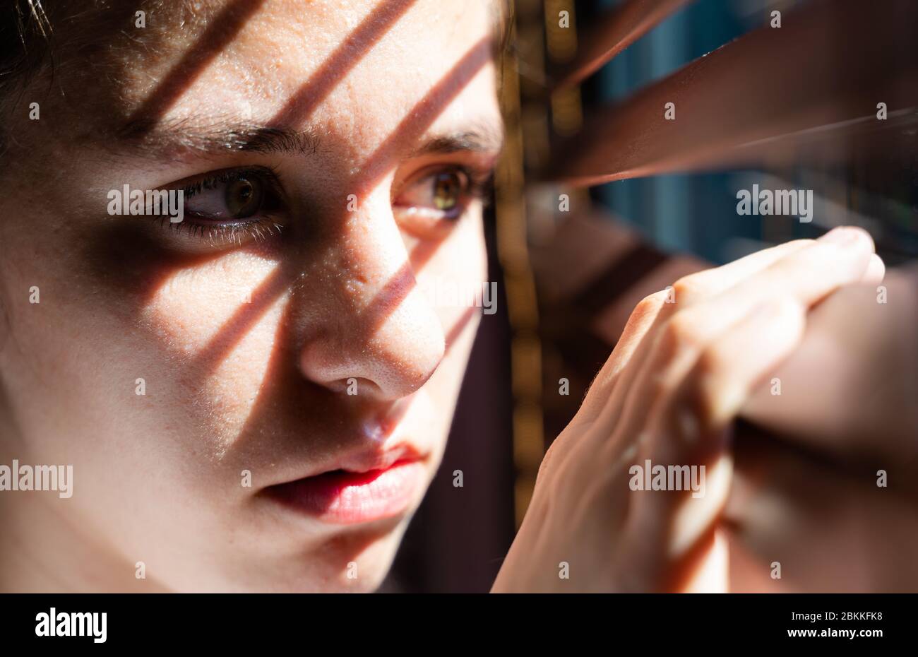 youth girl with green eyes opening a wooden curtain with her fingers to  look through the window while the sunlight creates sun and shadow on her  face Stock Photo - Alamy