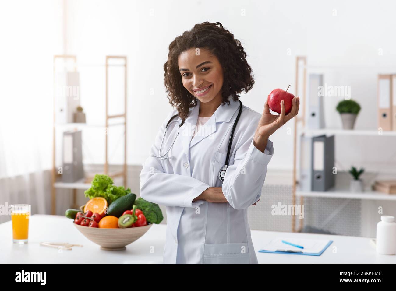 Positive female nutritionist posing at clinic, holding apple Stock Photo