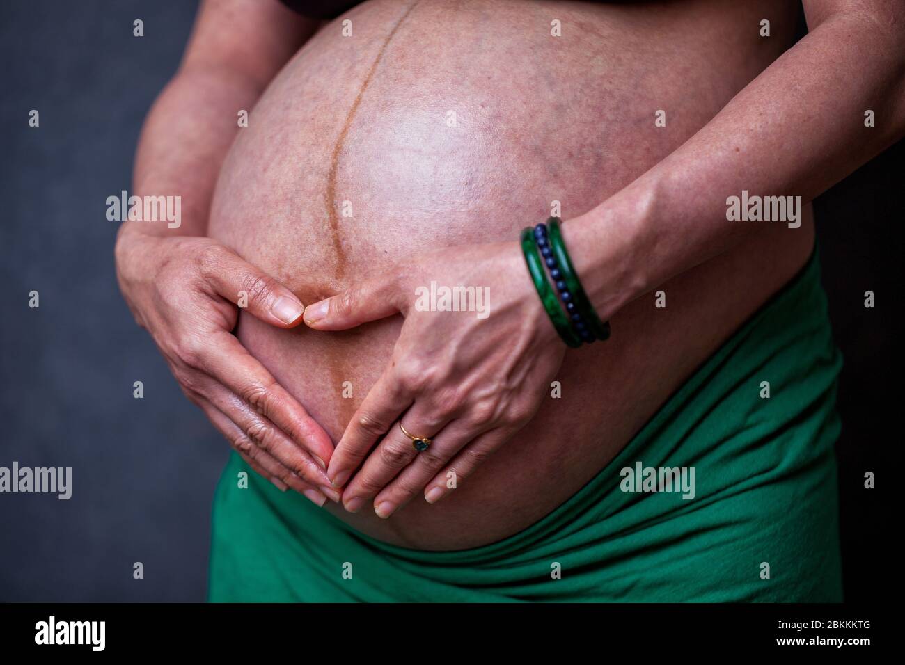 Stomach of a pregnant woman in the third trimester with her hands over fetus in the shape of a heart Stock Photo