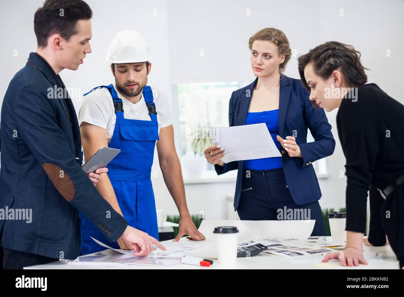 Four young business people working as a team gathered around a chart in an open plan modern office. Stock Photo