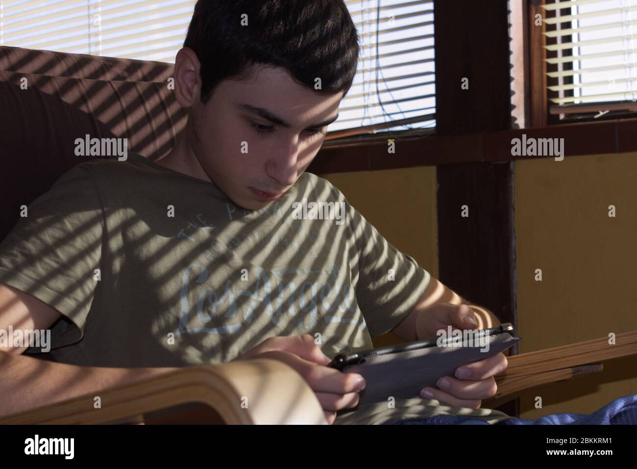 Caucasian boy sitting in an armchair checks his social networks on the tablet Stock Photo