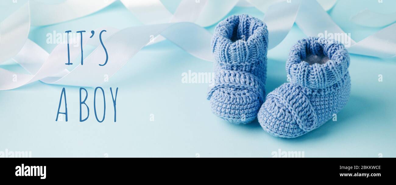 It's a boy text. Blue Baby knitted shoes for newborns on blue background, Minimal baby shower, newborn party background, copy space Stock Photo