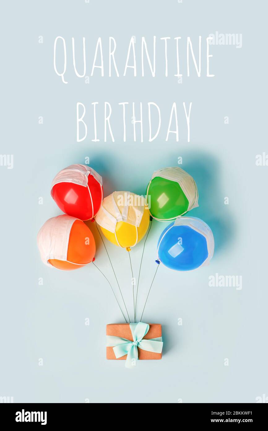 Quarantine birthday. Gift box hanging on air baloons and medical face mask. Social distance, isolation during coronovirus pandemic, virtual party onli Stock Photo