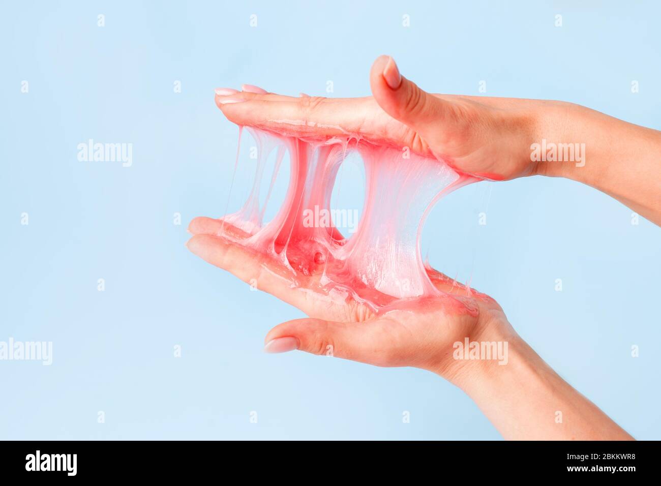 Young girl hands with sticky purple slime on blue background, liquid