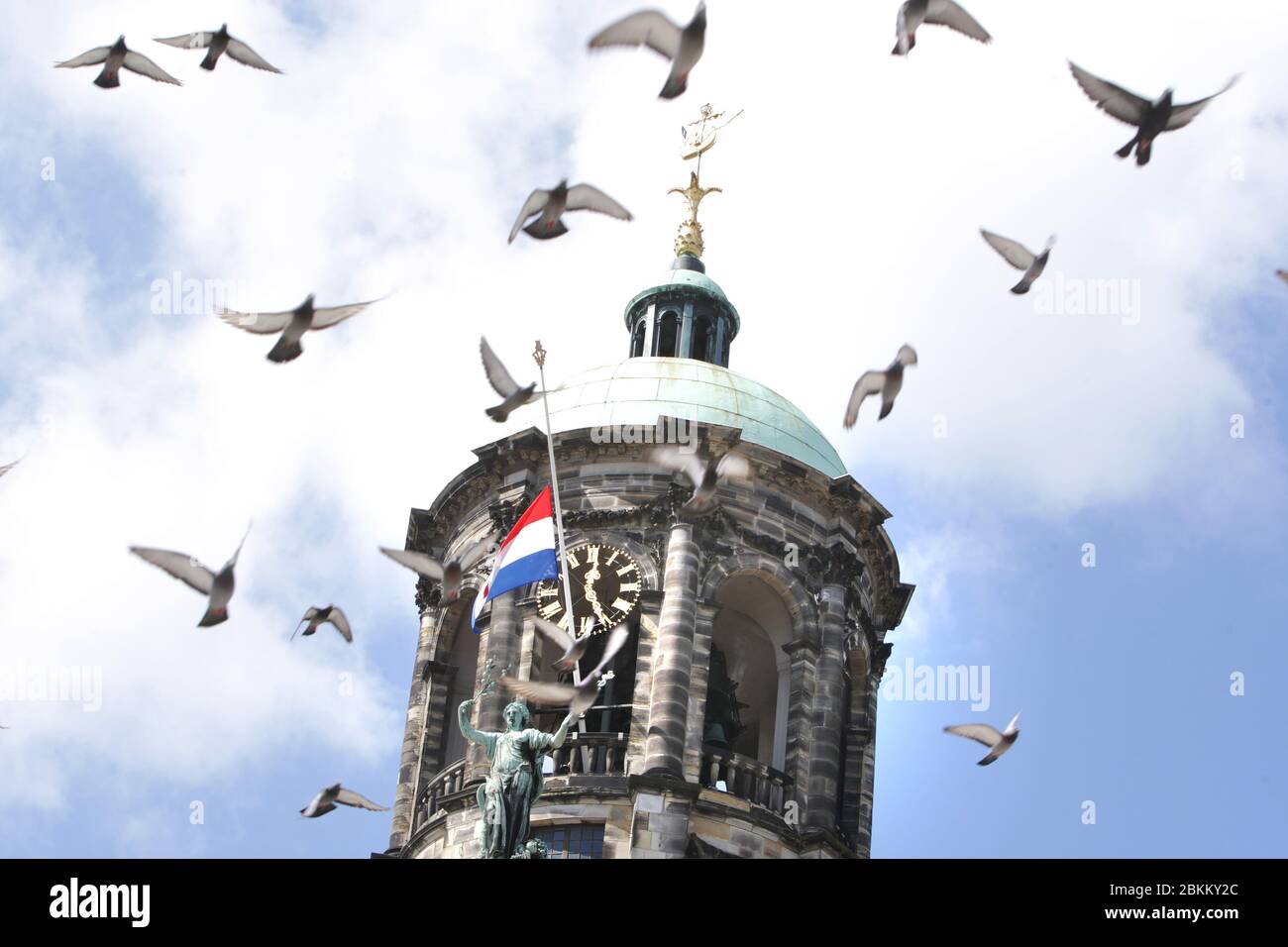Pegeons fly over the National Dutch flag flying at halfmast at the