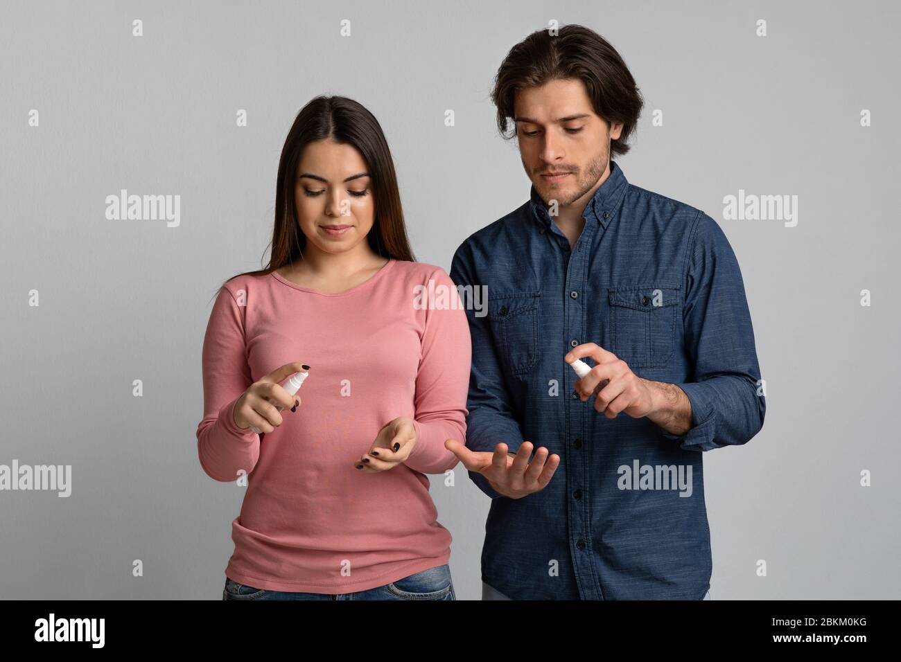 Precautions During Coronavirus Outbreak. Young couple applying disinfectant spray on hands Stock Photo