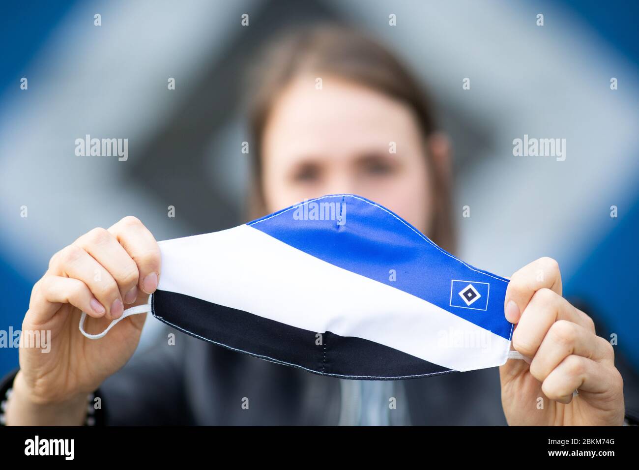 Hamburg, Germany. 04th May, 2020. An employee of Hamburger SV holds a  mouth-and-nose protection mask in the colours of HSV in front of the  Volkspark Stadium. Second division football club Hamburger SV