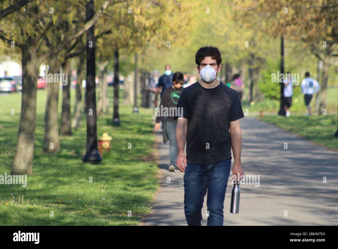 Jersey City, New Jersey, USA. 3rd May, 2020. This masked face man walks  alone down an alley in Liberty State Park in Jersey City while passing  other pedestrians. Residents have gathered in
