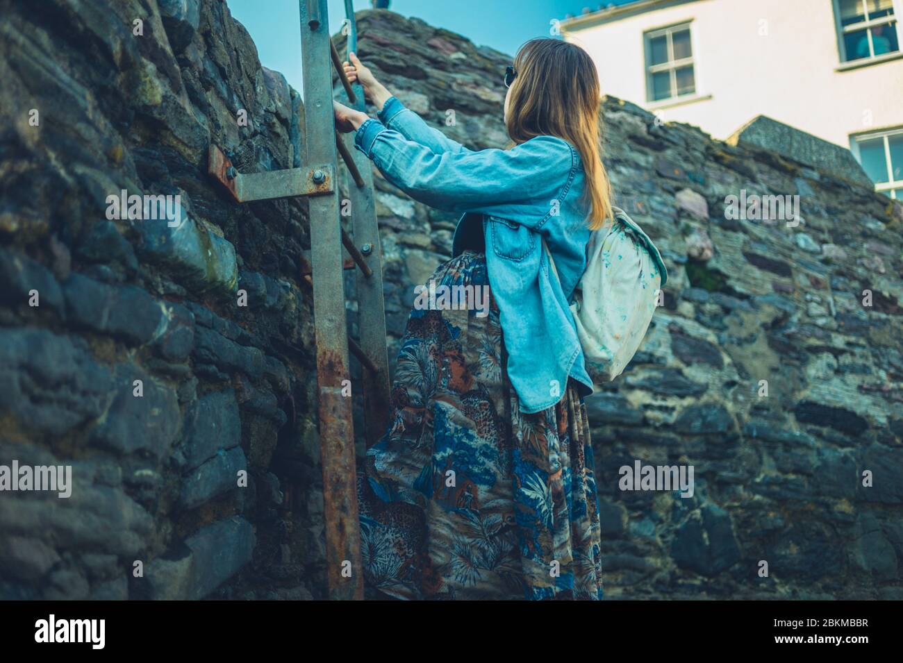 A young pregnant woman is climbing up a ladder outdoors Stock Photo