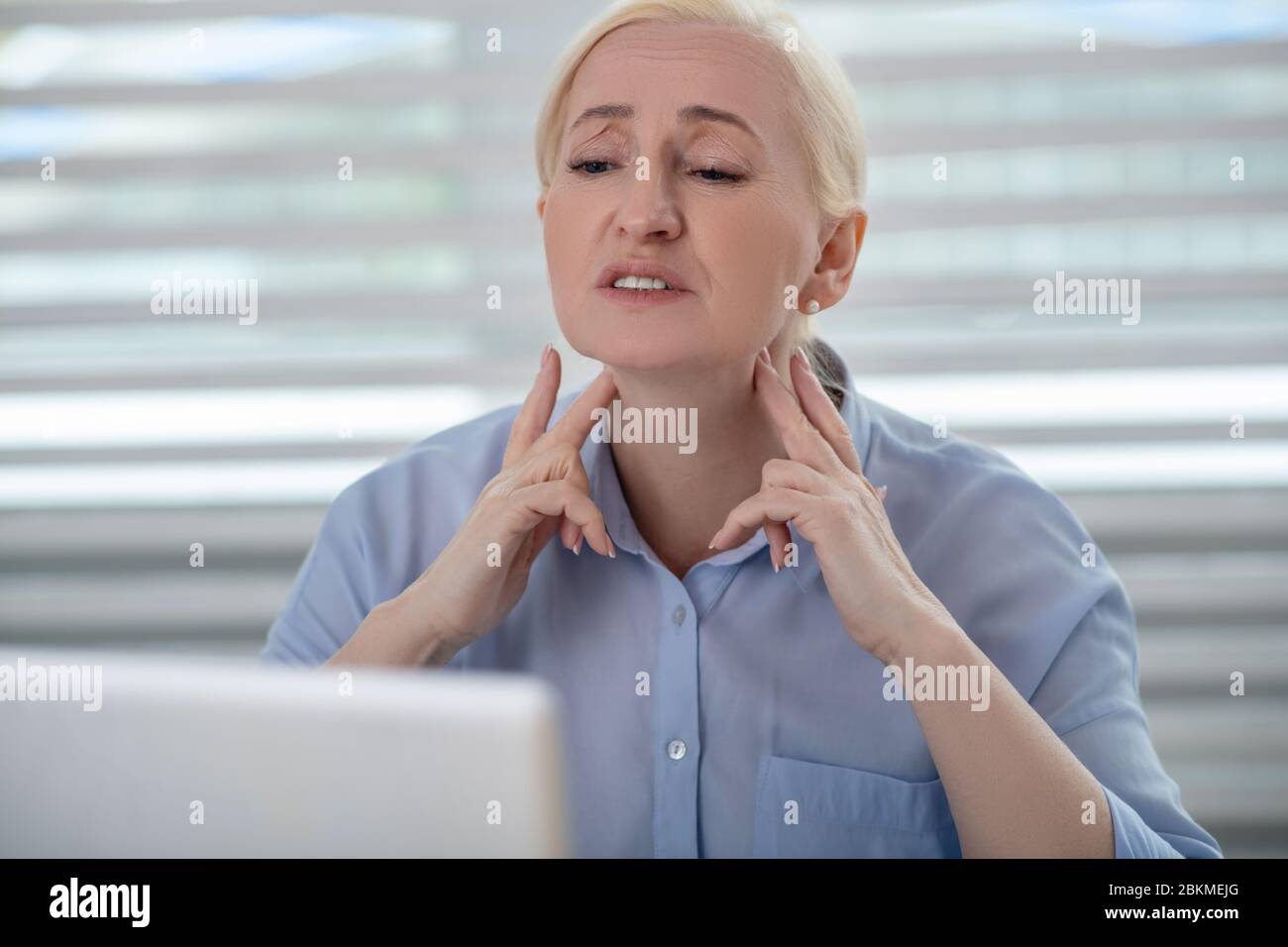 Woman in front of laptop monitor hands near neck Stock Photo - Alamy