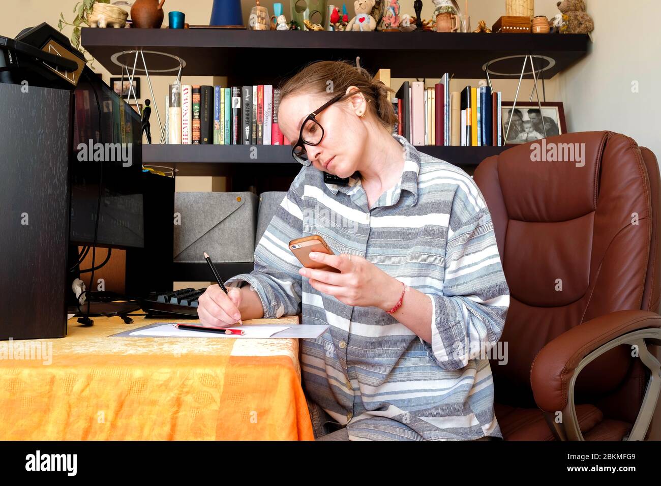 A woman works at home. Talks on the phone, records. Cozy atmosphere, home clothes. Stock Photo