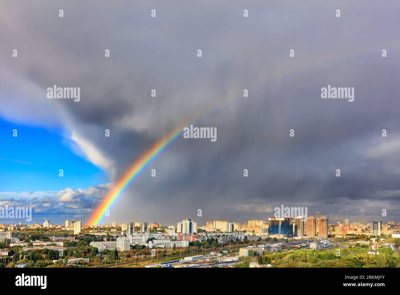 A bright rainbow in the sky above urban houses, sunlight displaces a thunderous front revealing a blue sky. The concept of change for the better. Stock Photo
