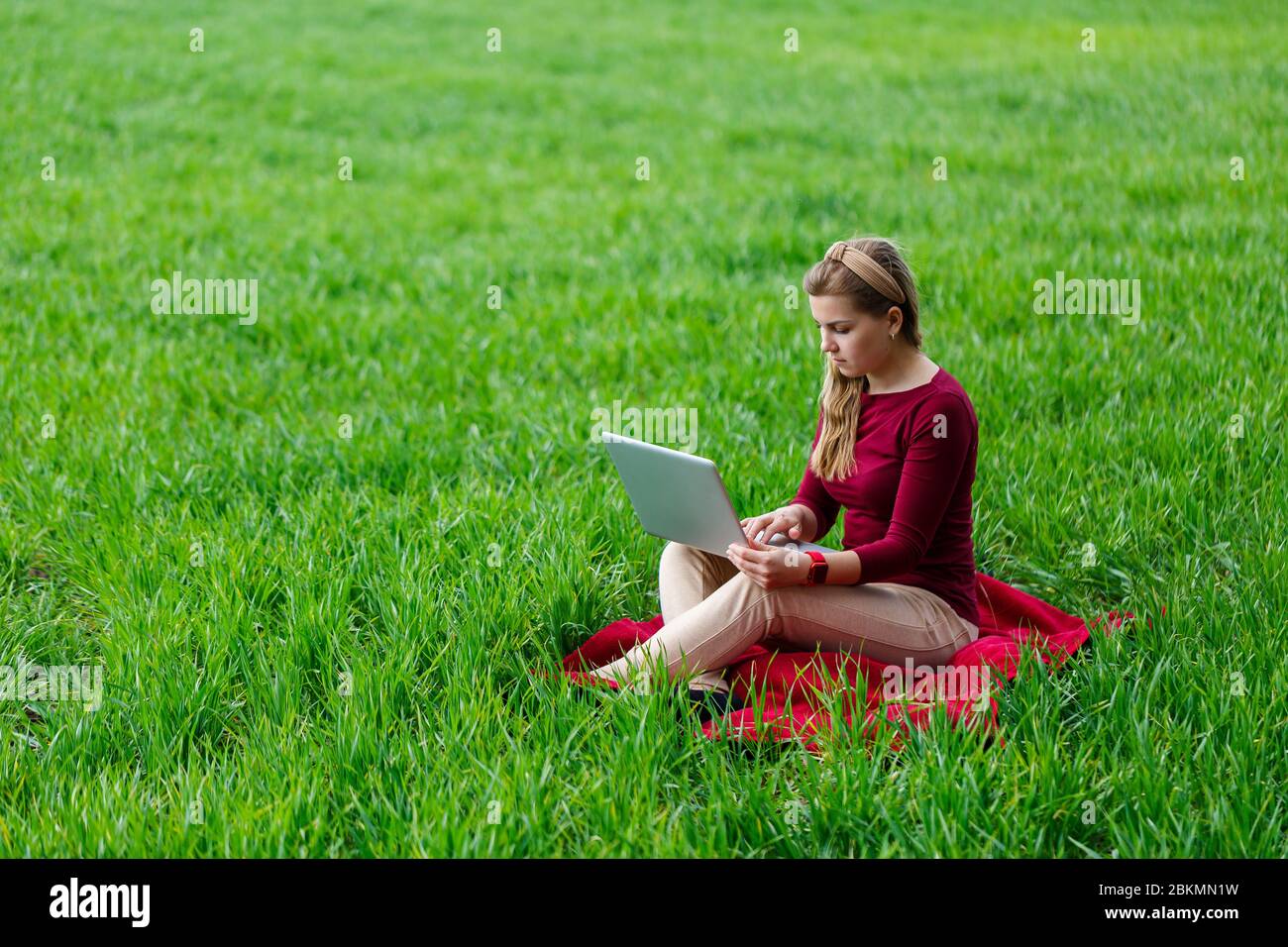 Young successful woman is sitting on green grass with a laptop in her ...