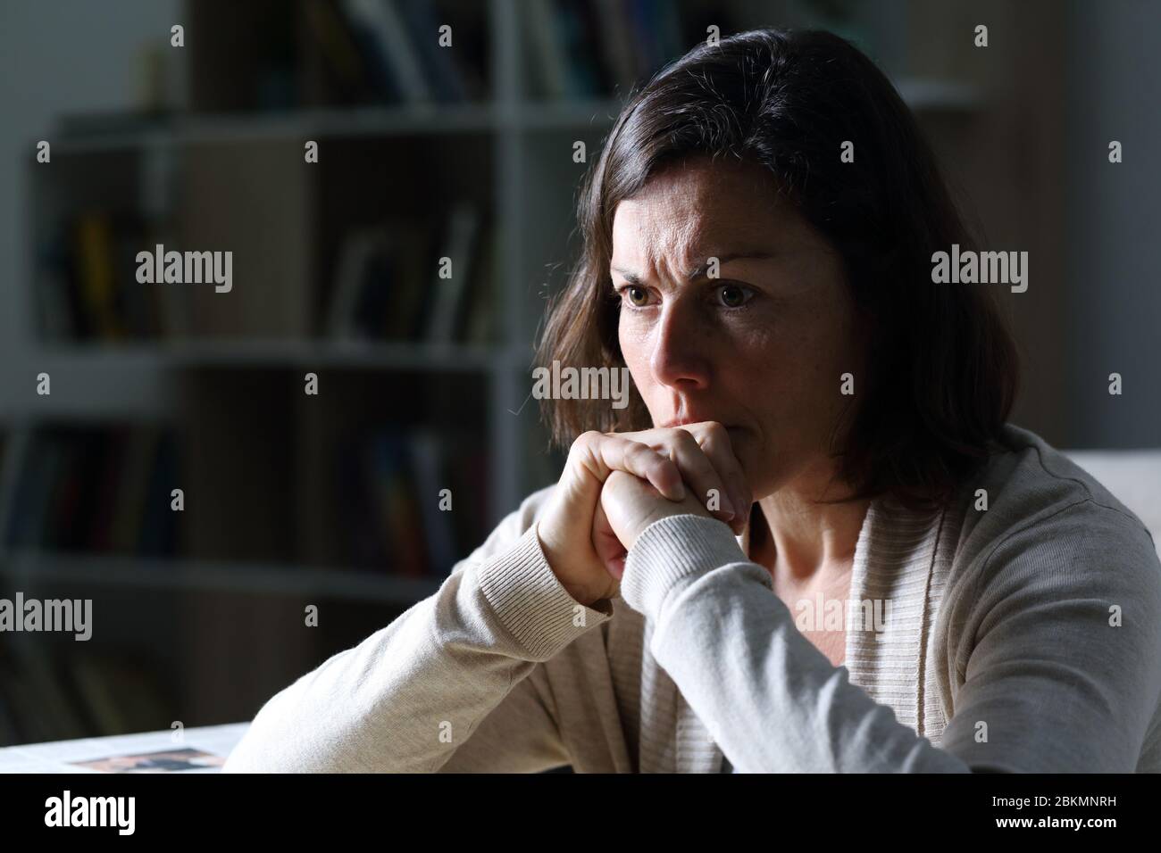 Angry middle age woman thinking looking away sitting alone at night in the livingroom at home Stock Photo
