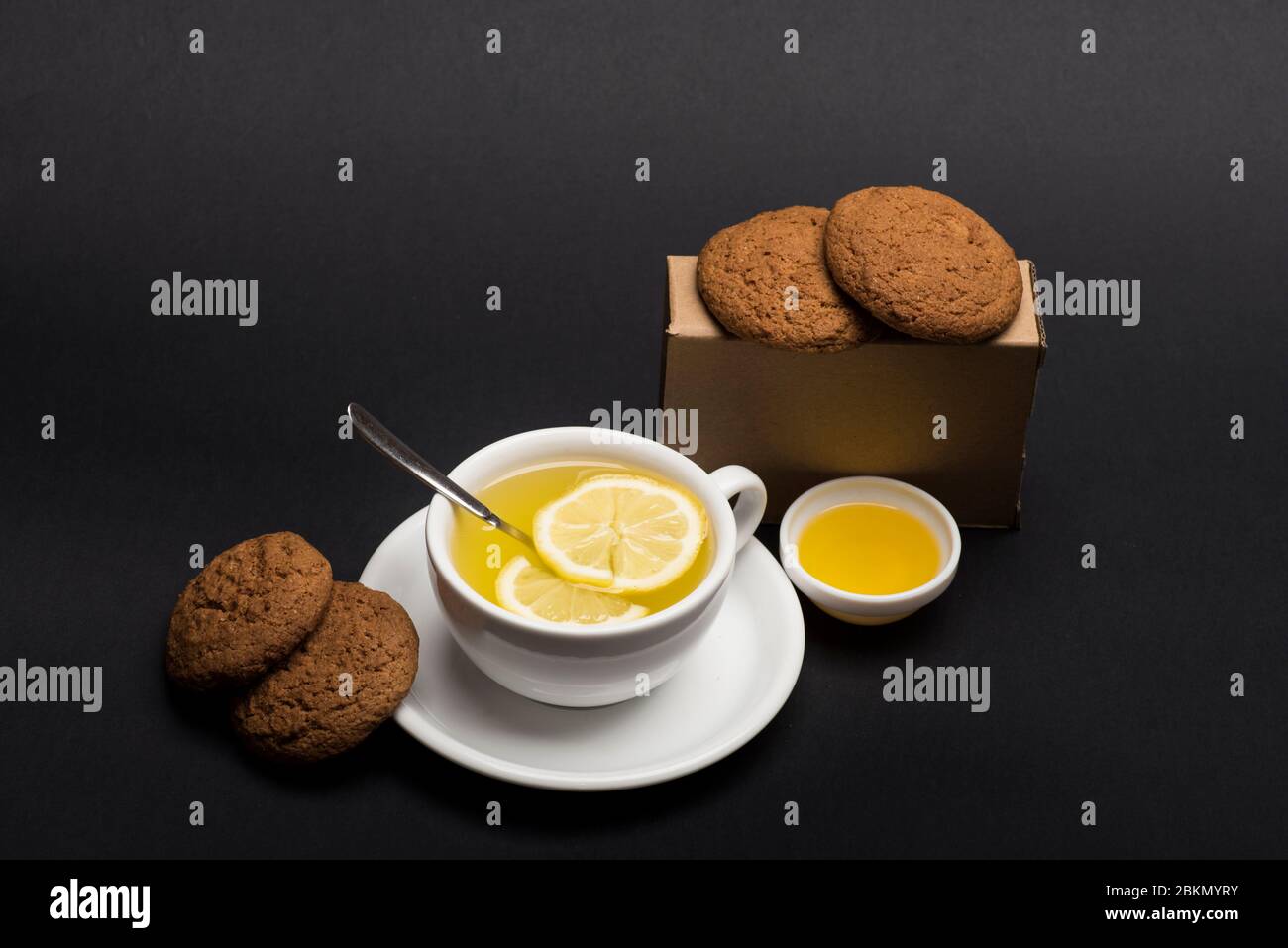 Nutrition And Hot Beverage Concept Cookies In Carton Box Near Tea On Dark Grey Background Sweet Bakery And Tea Time Oatmeal Biscuits As Tasty Pastry For Cup Of Tea With Lemon And