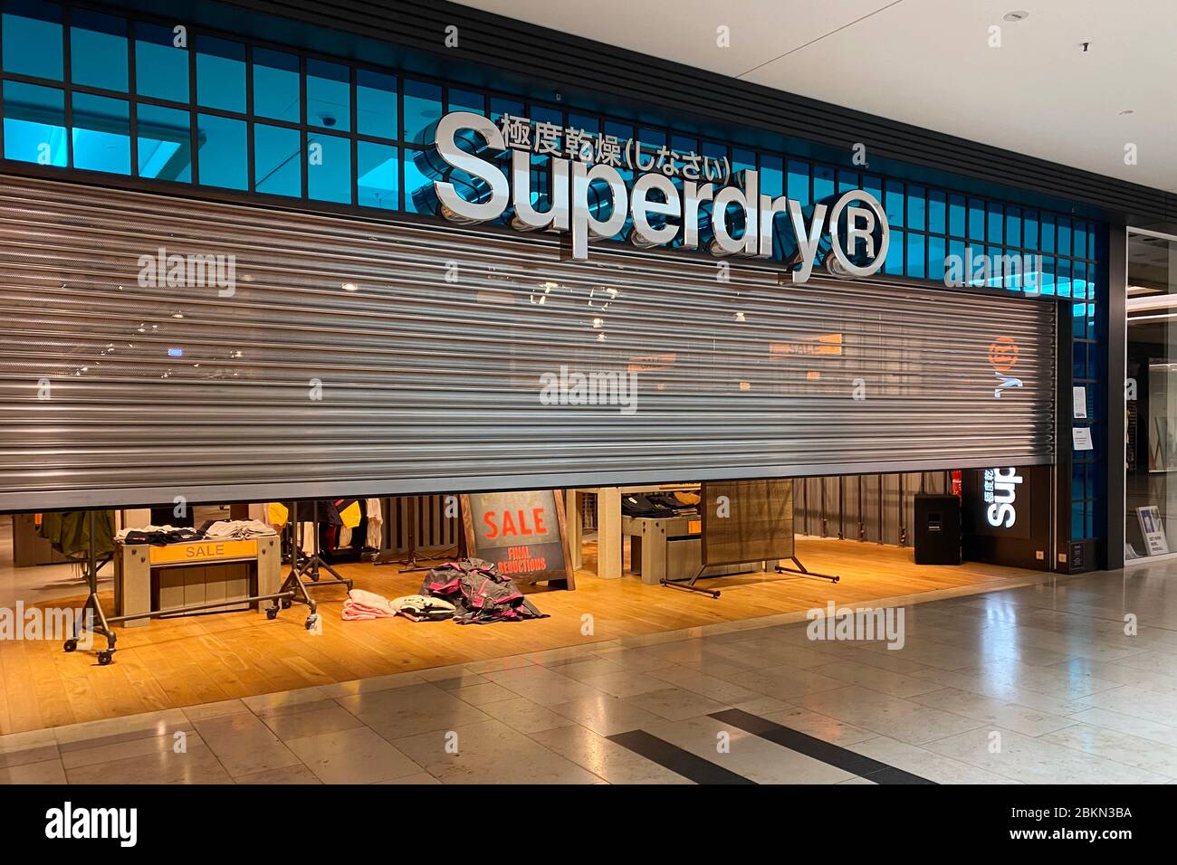 A fashion store (SUPERDRY) is preparing to reopen after loosening the  corona measures. The roller shutter in the shop is half open. Empty aisles  and escalators-closed stores, shops, shops. Closed shopping mall