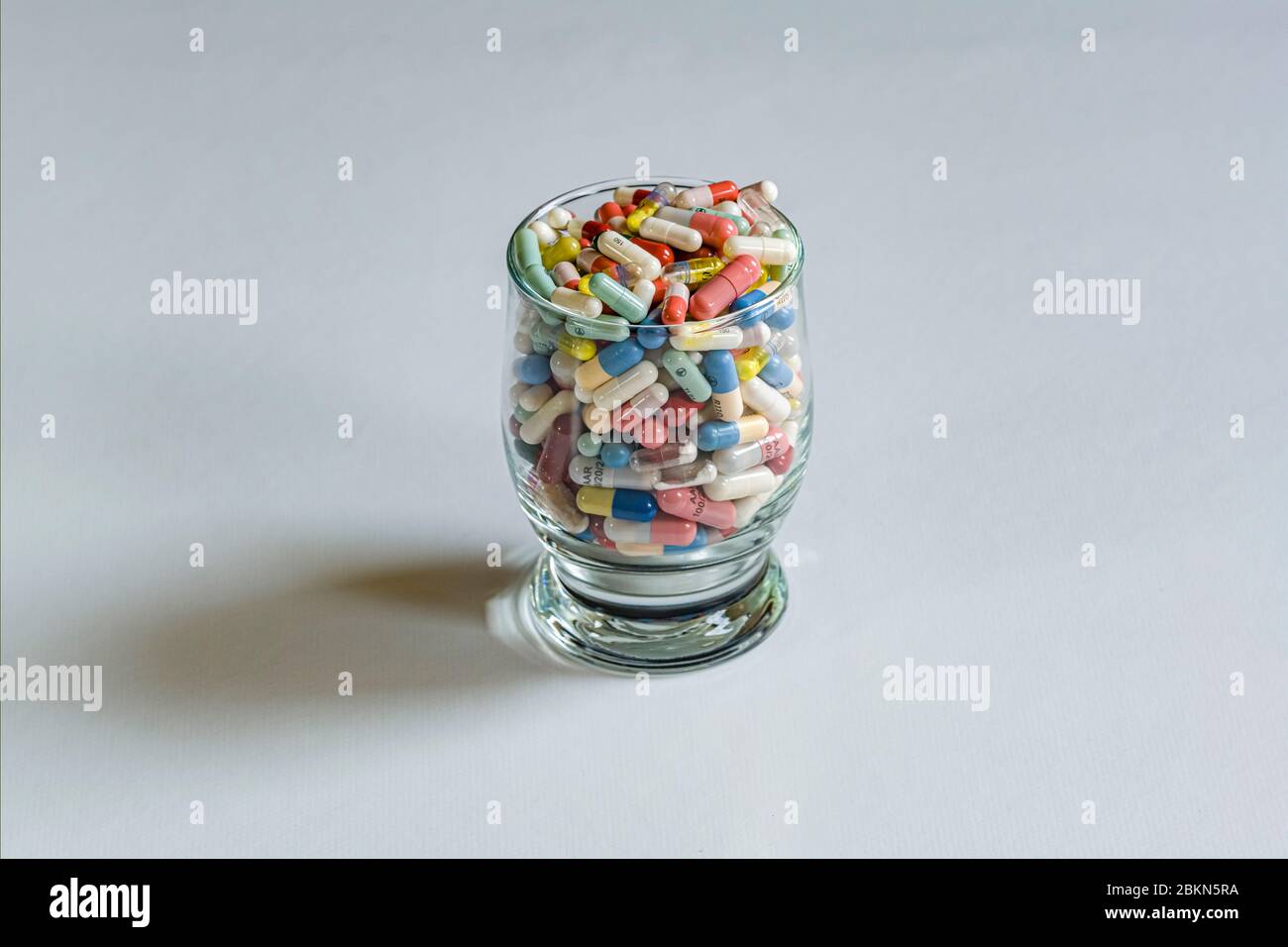 A cocktail glass filled with differently colored medical capsules, displayed on a white table Stock Photo