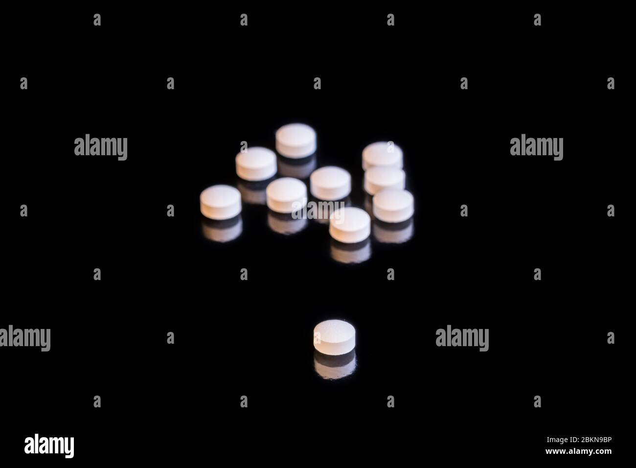 A small heap of white medical tablets, one tablet separated, displayed on a black table Stock Photo