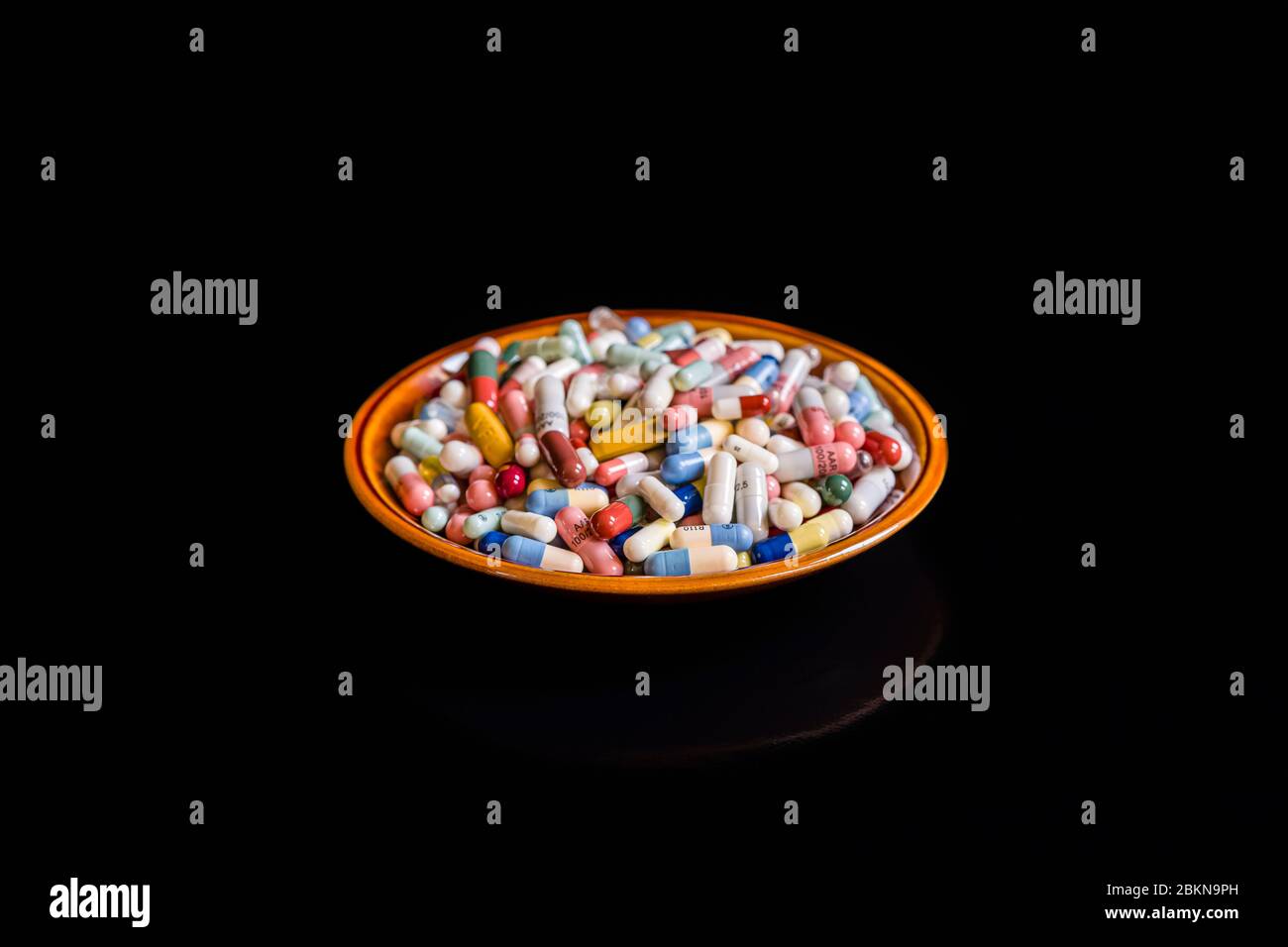 A small plate filled with differently colored medical capsules, displayed on a black table Stock Photo