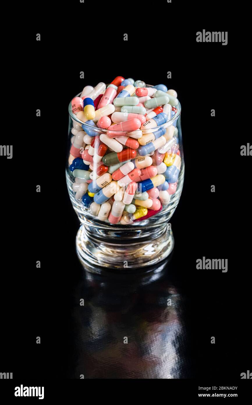 A cocktail glass filled with differently colored medical capsules, displayed on a black table Stock Photo
