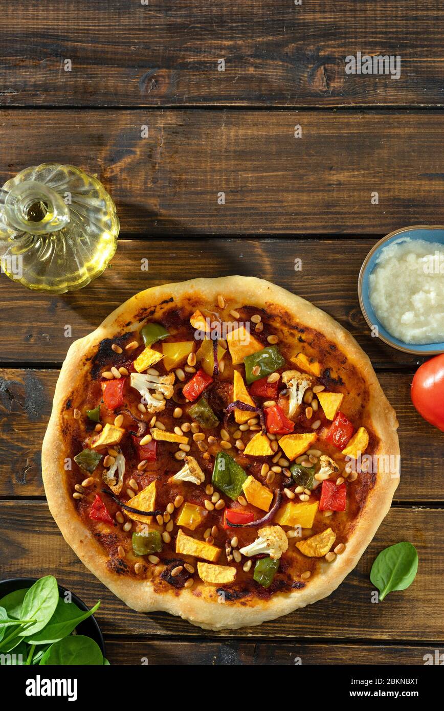 Vertical shot of delicious vegan pizza with tomato pesto, vegetables and pine nuts Stock Photo