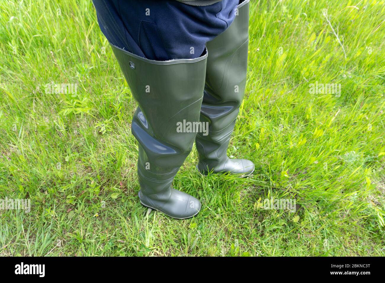 fisherman stands in rubber boots for a swamp in the river and holds a  fishing rod in his hand in the summer Stock Photo - Alamy