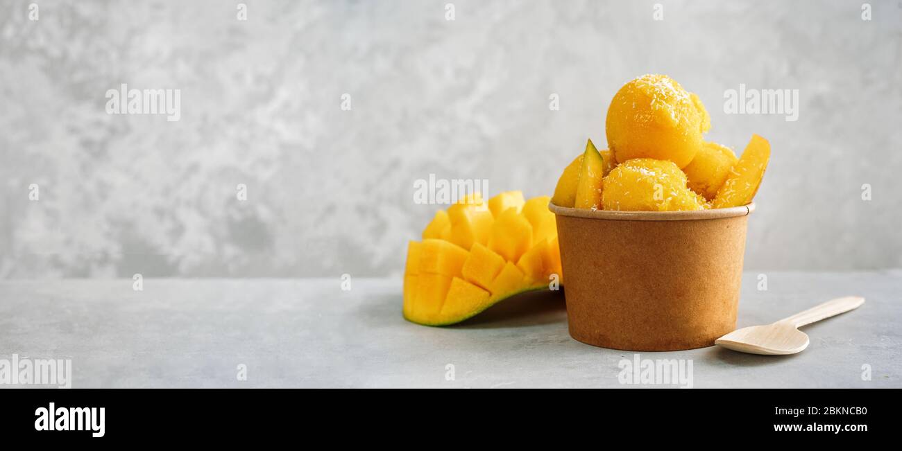 Refreshing mango ice cream in a paper paper cup on grey background Stock Photo